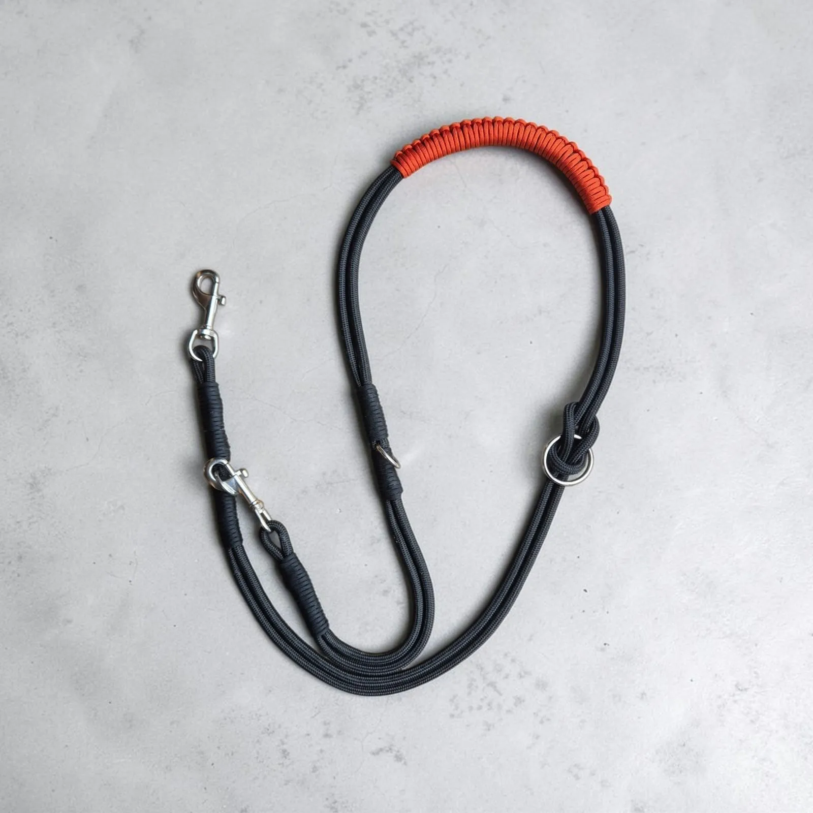 Black rope 3-in-1 dog lead laid flat with an orange braided handle and stainless steel clips